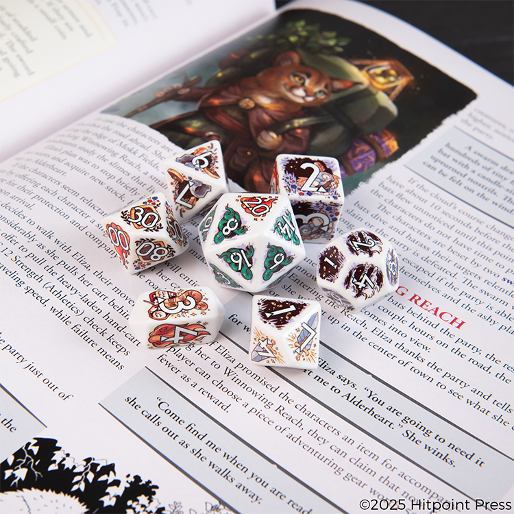 Set of ornate polyhedral dice with a Humblewood design on an open book with fantasy illustrations of humblewood. 
