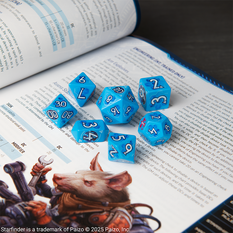 Set of ornate polyhedral dice with a Starfinder / Scifi design on an open Starfinder book. The base color of the dice are a medium / dark blue, the numbers are white. 